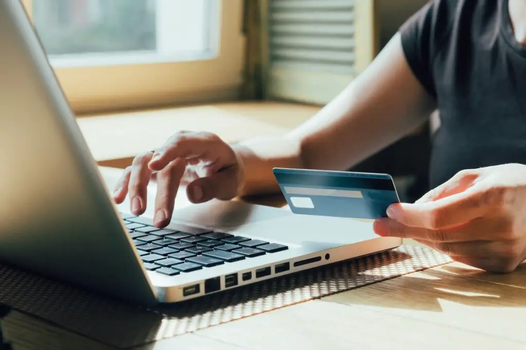 A person typing something on the laptop while holding a credit card