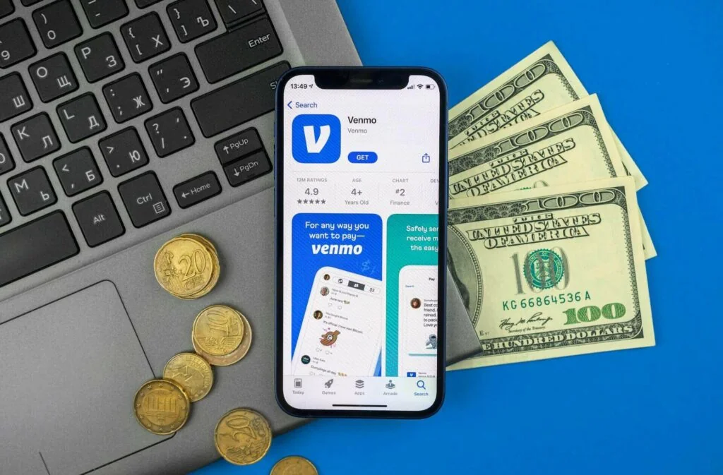 App store open on a smartphone, next to some cash and a laptop