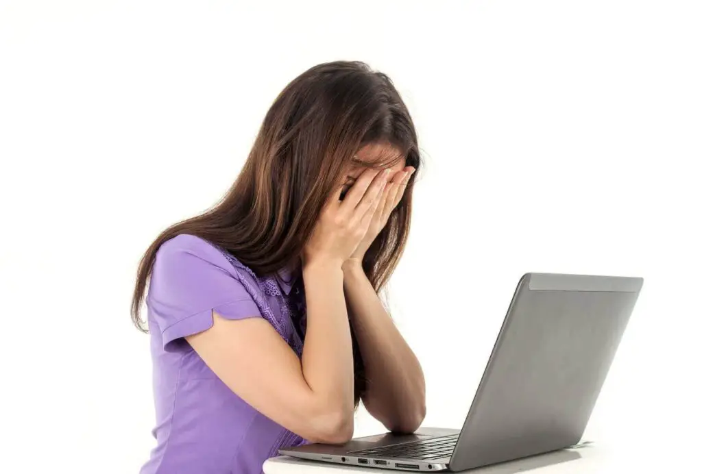 Woman covering her face while looking at a laptop